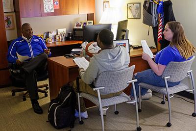 two students sitting with an advisor in office