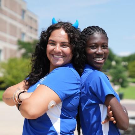 two students in central uniforms posing back to back outside