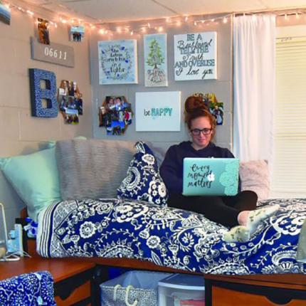 student in decorated dorm room on laptop