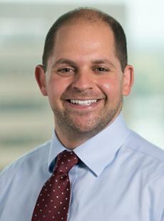 A headshot of a balding Caucasian man with brown hair wearing a dress suit and tie.