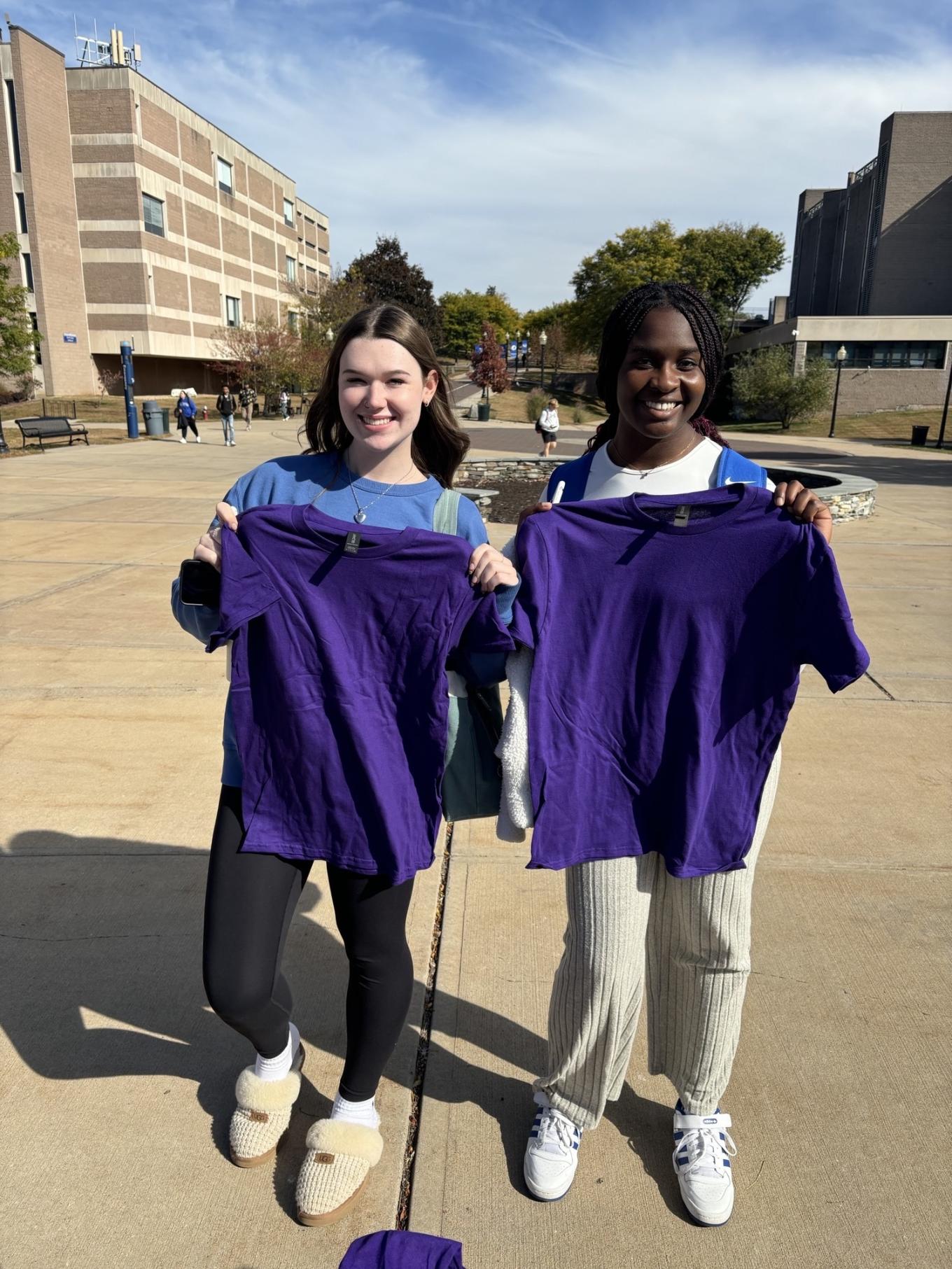 Duo holding up purple shirts