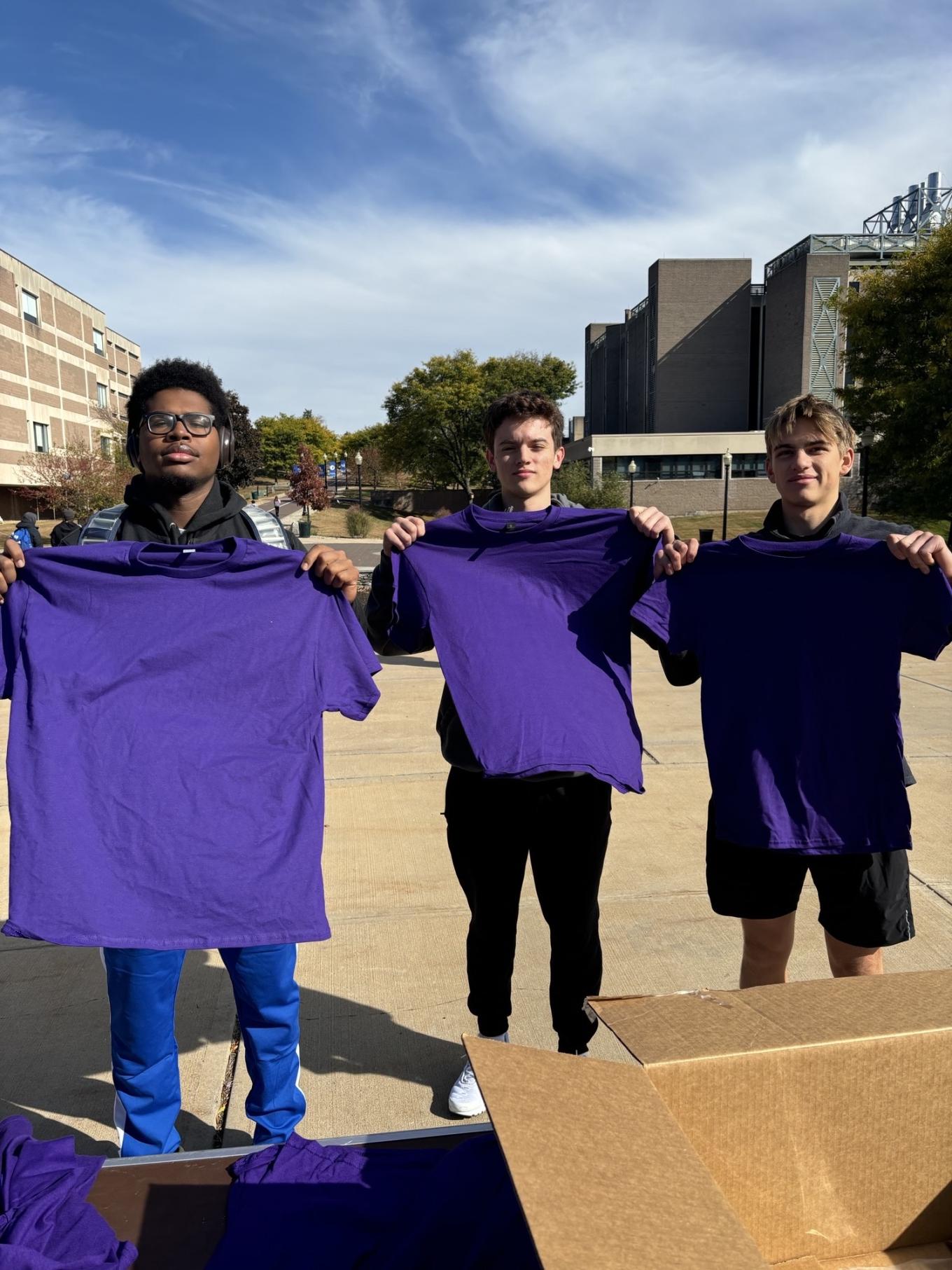 Trio holding up purple shirts